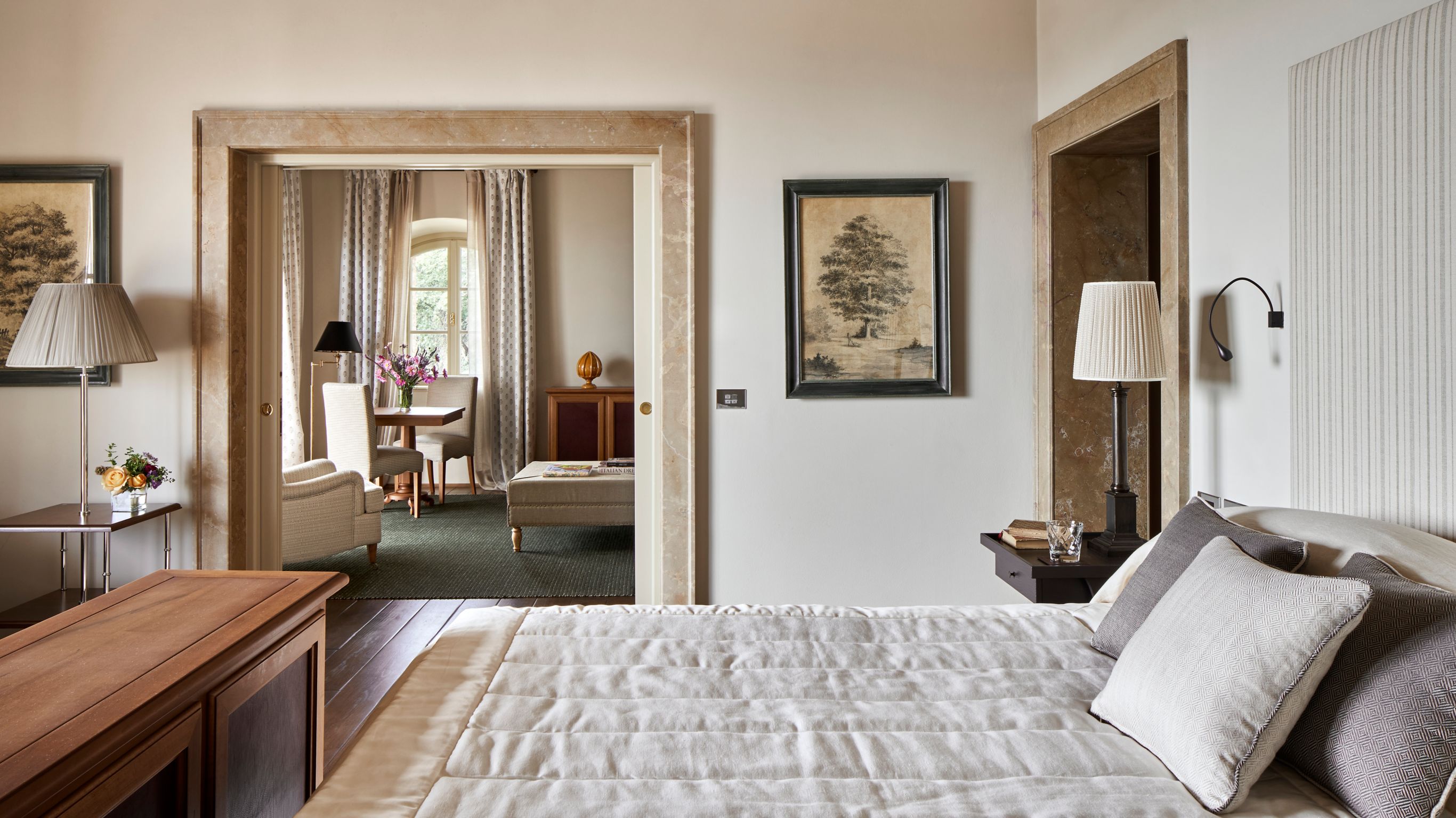 A bedroom with a neatly made bed, bedside tables, and a doorway leading to a sitting area